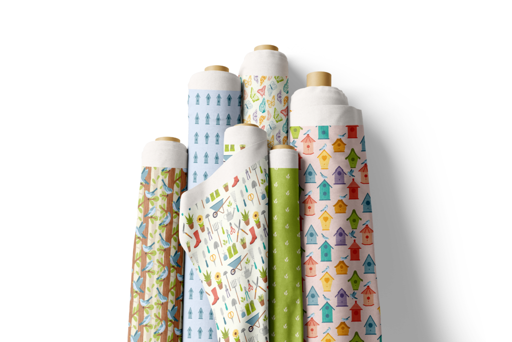 Six rolls of fabric leaning against the wall. Fabric is of spring patterns with birds, butterflies, bird houses, flowers and plants.