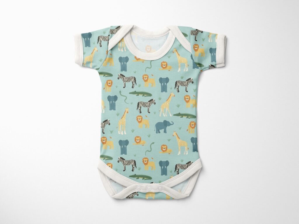 Photograph of baby onesie featuring a design of all the wild life animals like giraffes, lions, zebras and elephants on a blue background. 