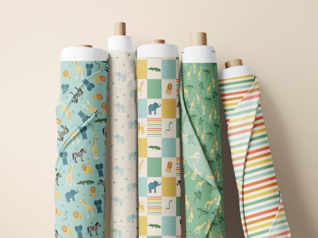 Five rolls of fabric leaning against a wall. Fabric designs features safari animals like giraffes, elephants, lions, zebras, crocodiles and snakes.